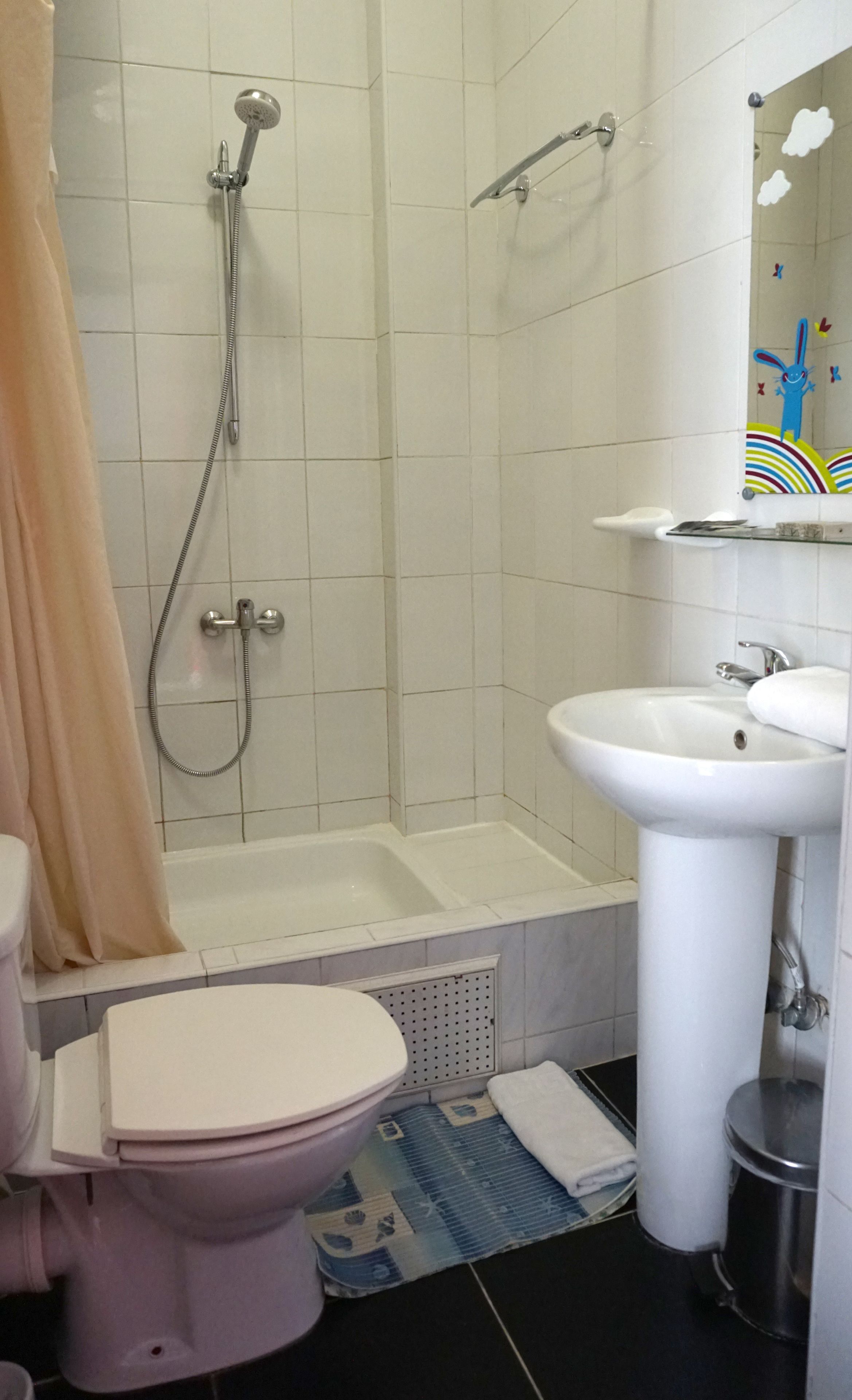 A bathroom with a toilet, sink, shower, and a mirror with a cartoon character.