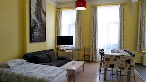 En stue med sofa, sofabord, fjernsyn, spisebord med stole og et maleri af Eiffeltårnet.