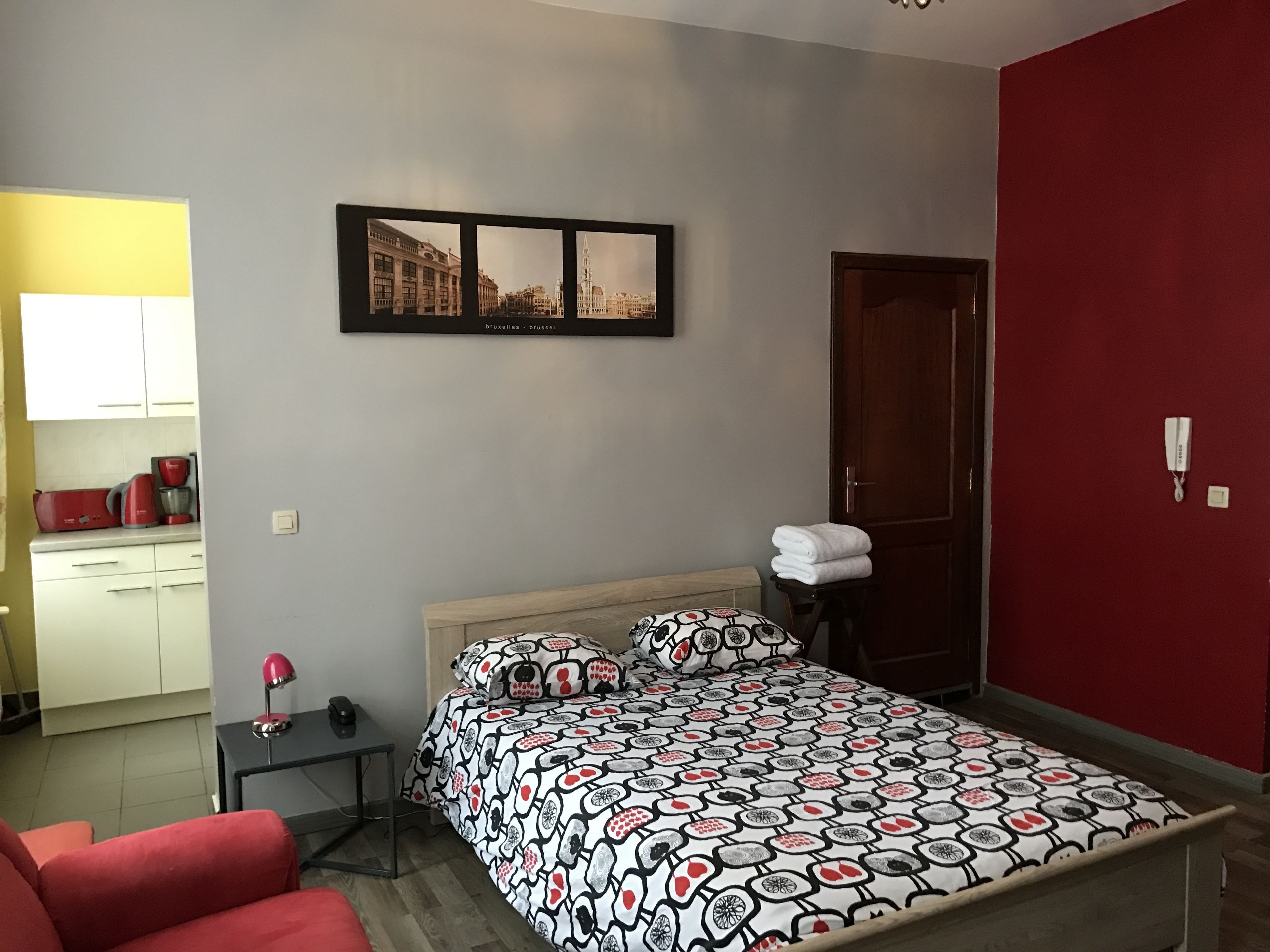 Une chambre à coucher avec un lit, une table de chevet, une chaise, un mur rouge et une porte.
