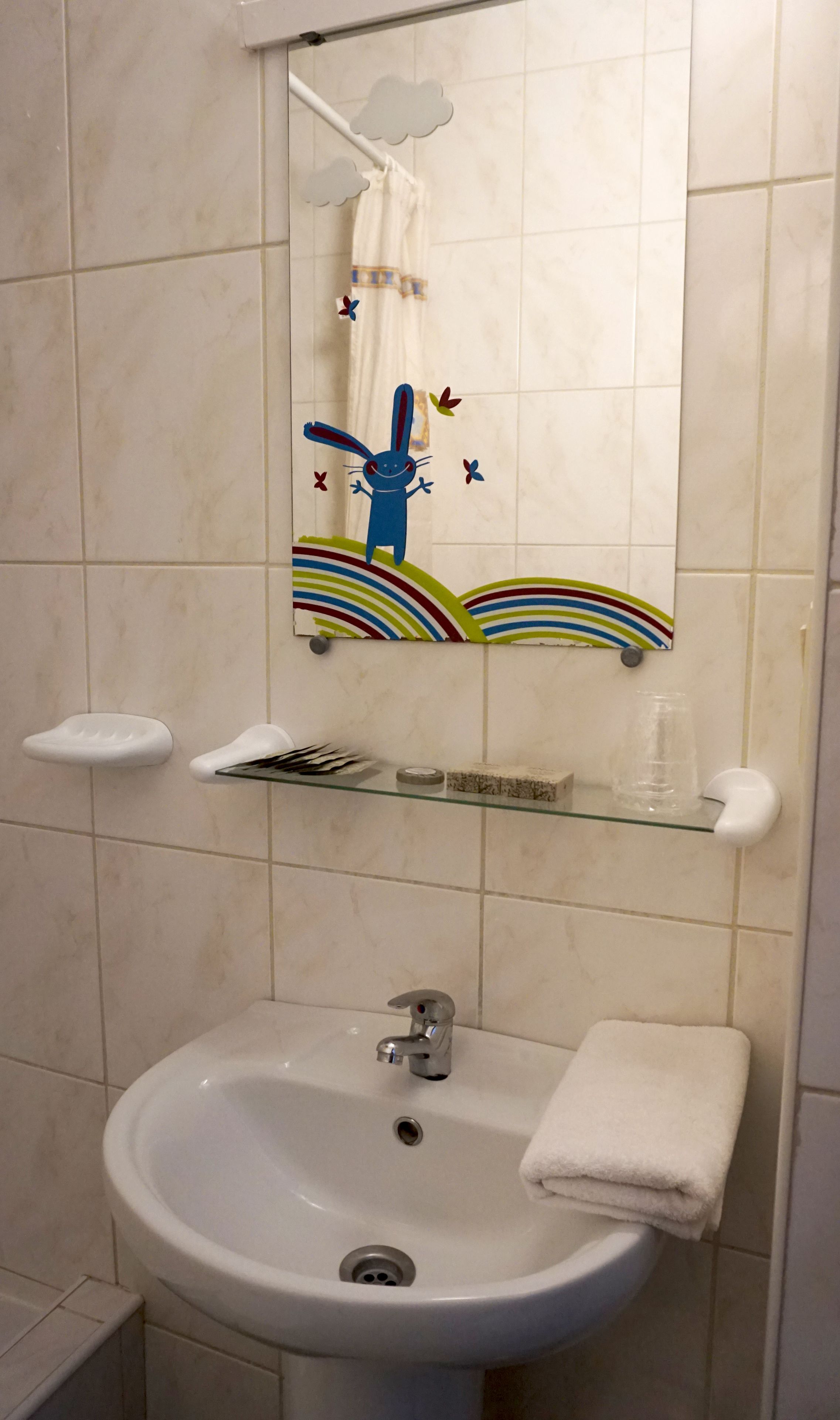 Une salle de bain avec un lavabo blanc, un miroir et une étagère contenant des articles de toilette.