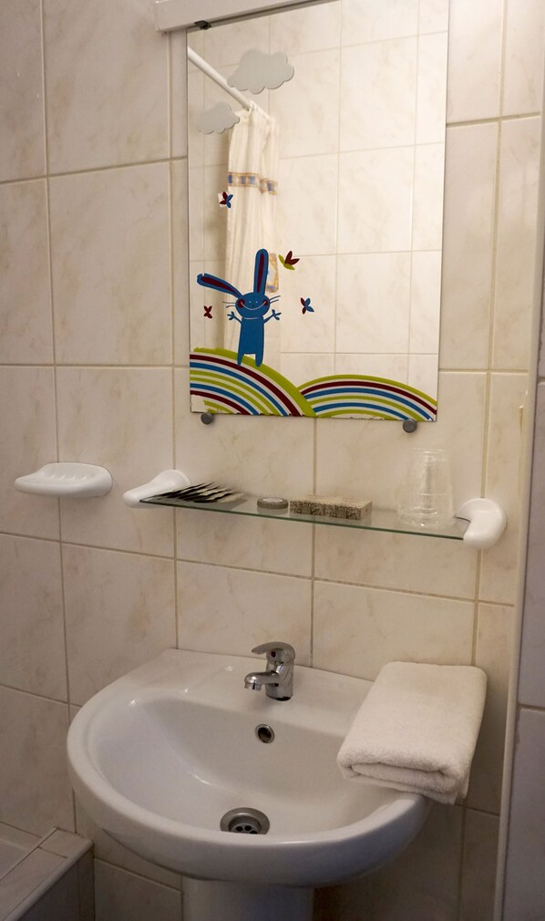 Un baño con un lavamanos blanco, un espejo y una repisa con artículos de aseo.