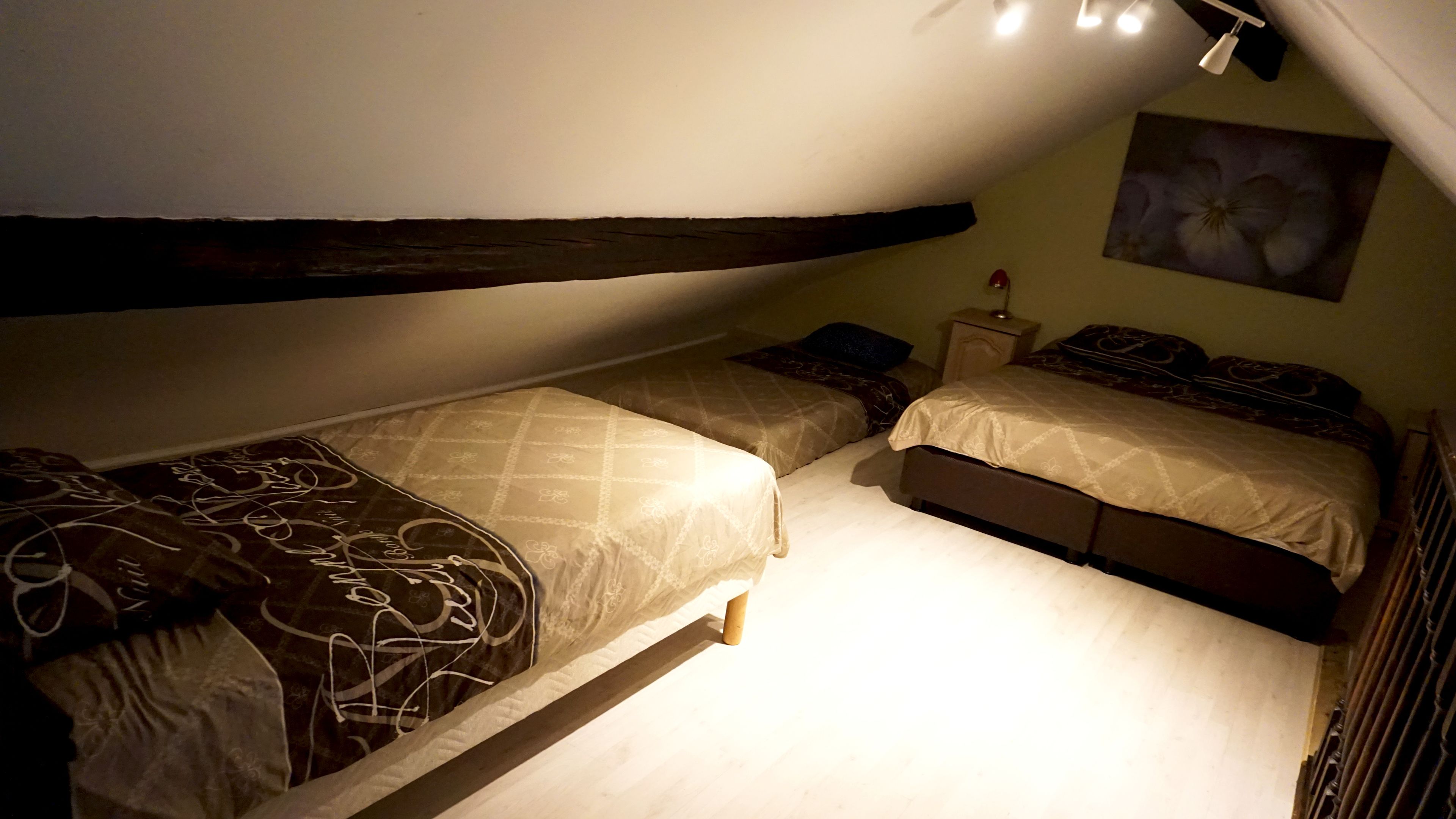 Een kleine, zwak verlichte kamer met twee eenpersoonsbedden, een nachtkastje en een wandlamp.