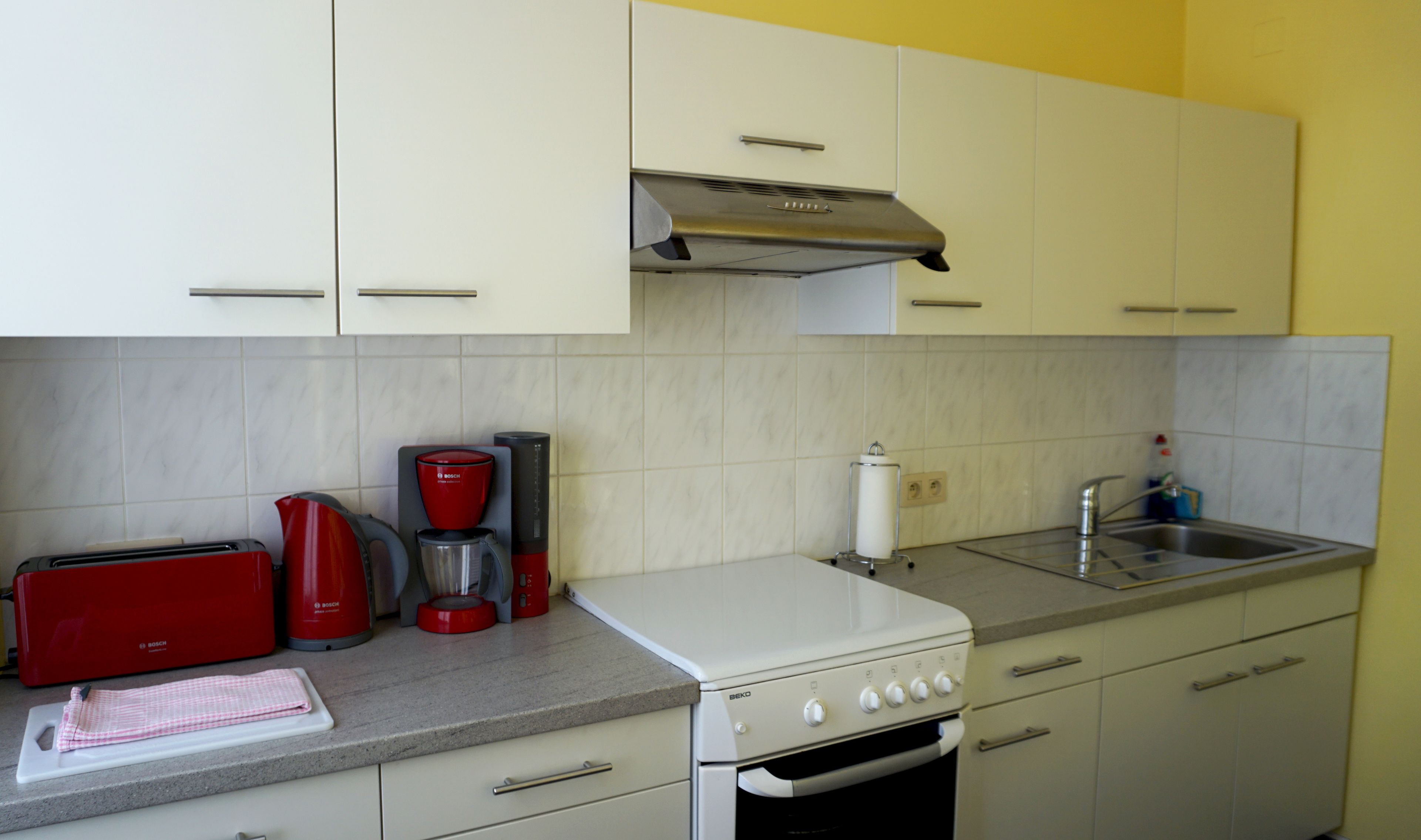 A kitchen with white cabinets, a Bosch coffee maker, a toaster, and a sink.