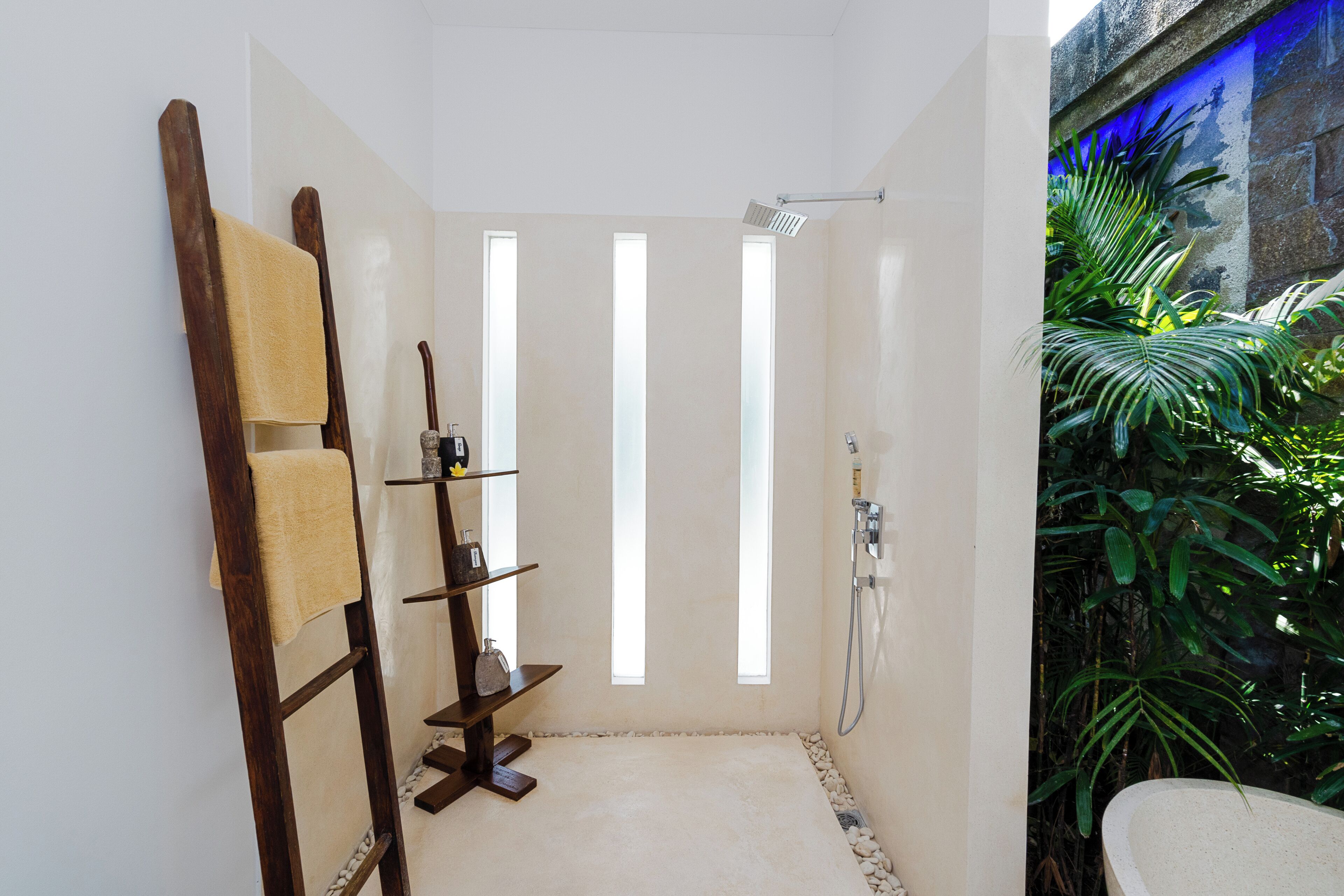 Un baño con una escalera de madera, estantes, ducha y vistas a la vegetación.