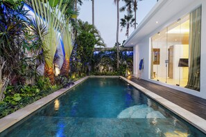Piscina rodeada por plantas tropicais e um edifício moderno com amplas janelas.