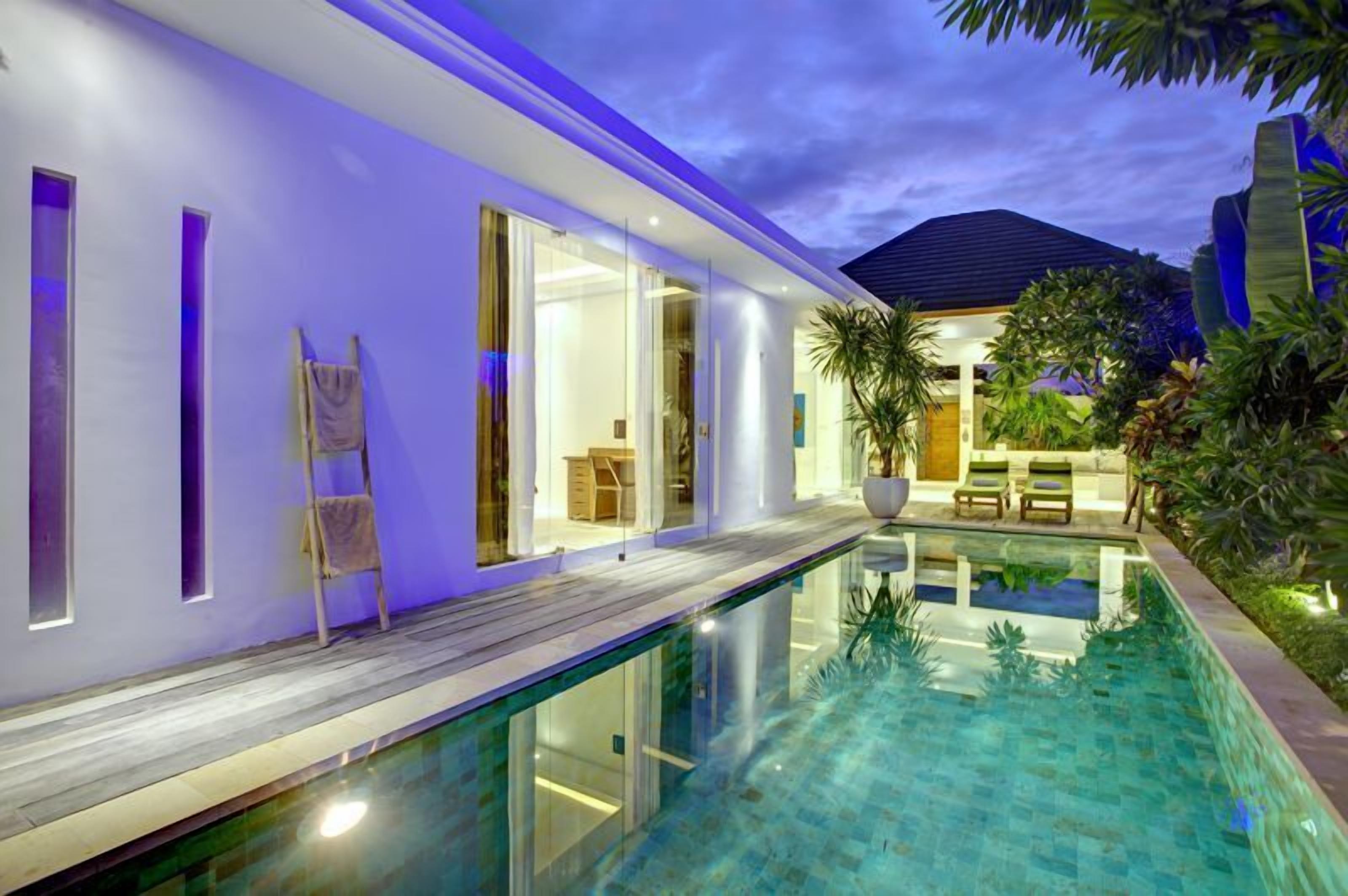 Et moderne hus med swimmingpool, træterrasse og et godt oplyst interiør.