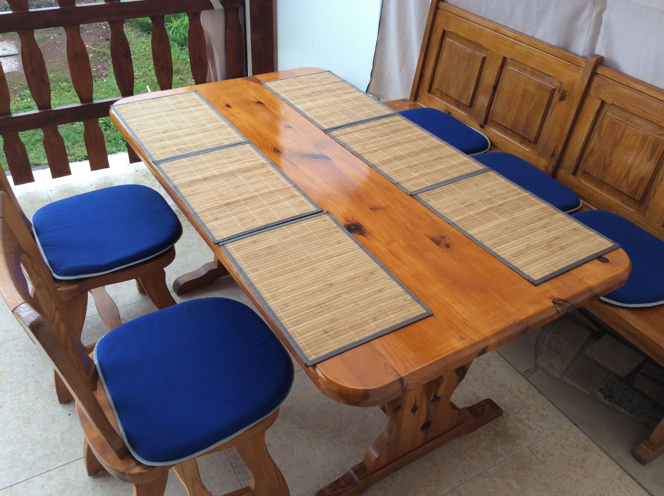 A wooden dining table with blue cushioned chairs and woven placemats.