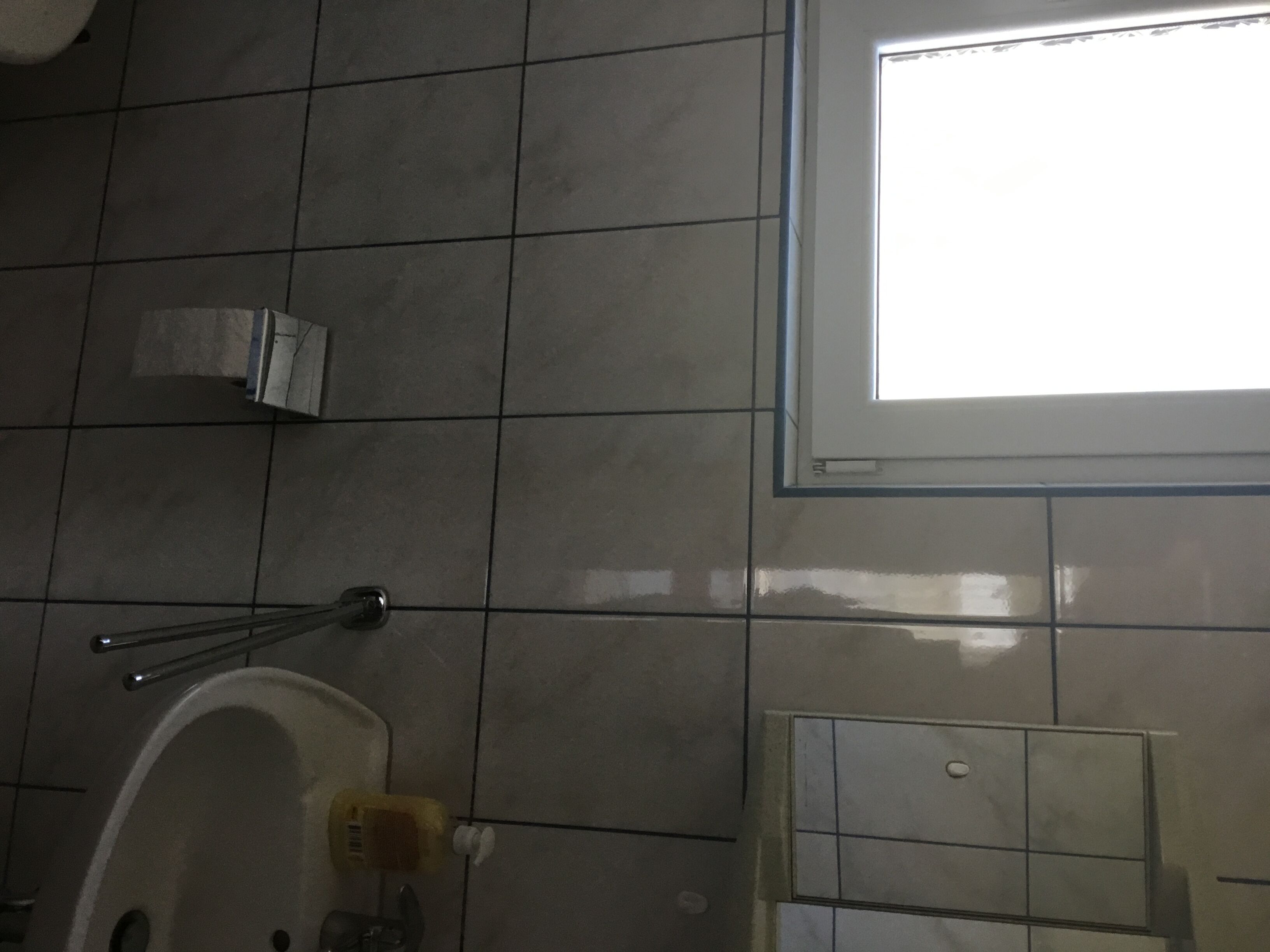 Une salle de bain avec un sol carrelé, un espace douche, des toilettes et une fenêtre qui laisse entrer la lumière naturelle.