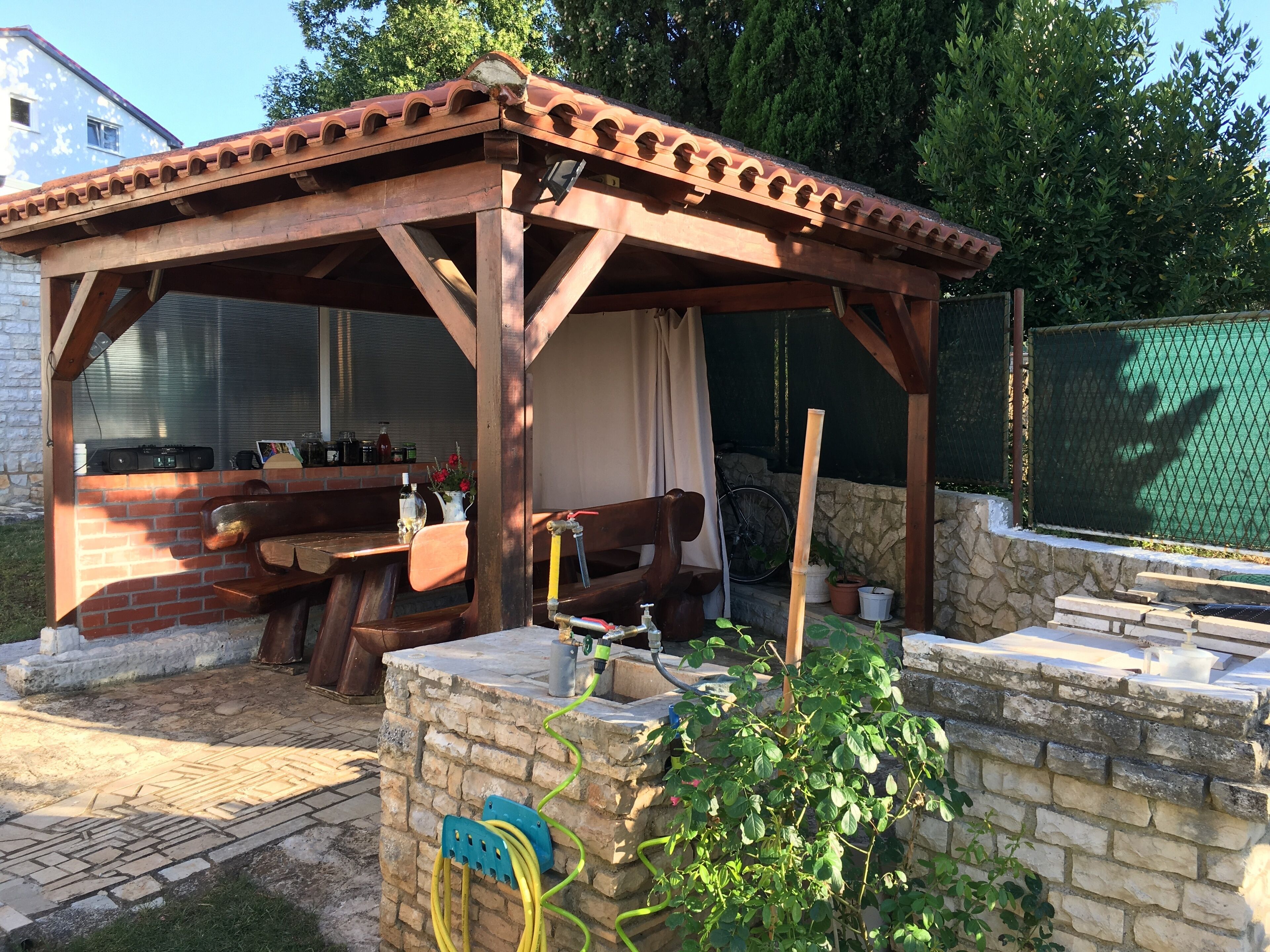 A wooden gazebo with a brick wall, a table, and chairs.