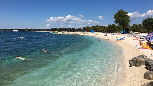 A beach with clear water, people swimming and sunbathing, and a boat in the distance. - Apartment for 2 people and 2 children (Pula)