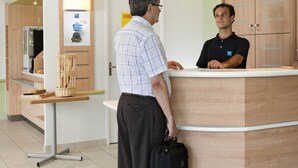 A reception area with a wooden reception desk, a counter, and a wall-mounted sign. - Ibis Budget Frankfurt Offenbach Sued (Offenbach am Main)