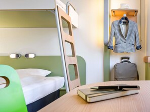 A bunk bed with a green headboard, a bedside table with a book and pen, a suitcase, and a hanging coat rack with a striped jacket. - Ibis Budget Frankfurt Offenbach Sued (Offenbach am Main)