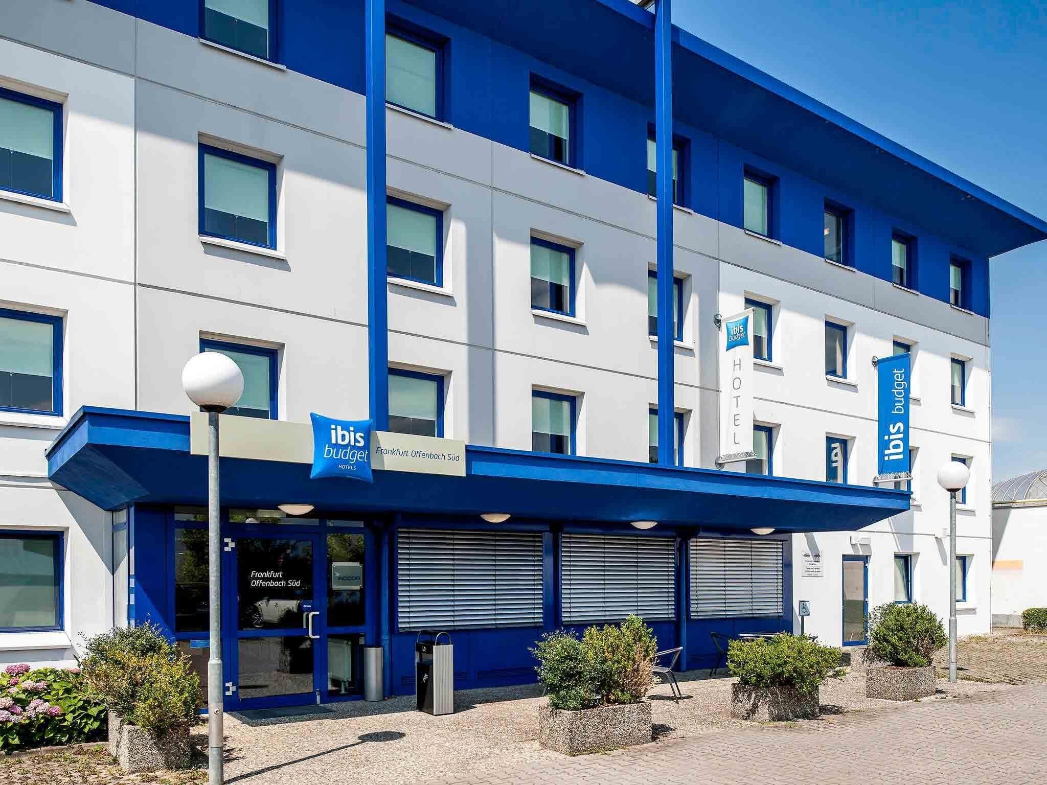 Un hôtel moderne, avec une façade bleue et blanche, de nombreuses fenêtres et une enseigne indiquant qu’il s’agit d’un hôtel ibis budget.