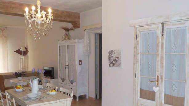 A dining area with a wooden table set for four, a chandelier, a cabinet, and a door with decorative glass panels. - Loft a few steps from the sea (Pozzallo)