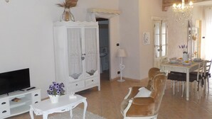 A living room with a TV, white furniture, a chandelier, and a dining area with a table and chairs. - Loft a few steps from the sea (Pozzallo)