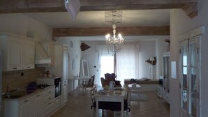 A spacious kitchen with white cabinets, a dining table, and a chandelier. - Loft a few steps from the sea (Pozzallo)