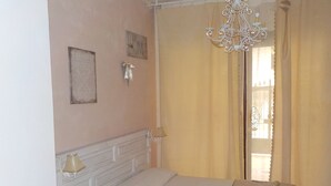 A bedroom with a bed, a chandelier, a window with curtains, and wall decorations. - Loft a few steps from the sea (Pozzallo)