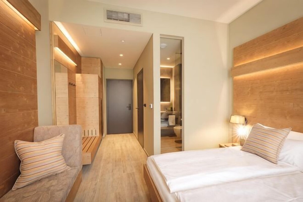 A hotel room with a bed, a sofa, a nightstand, and a bathroom visible through an open door.