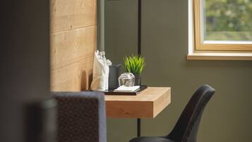 A modern room with a wooden bench, a desk with a lamp, a potted plant, and a view of greenery outside.