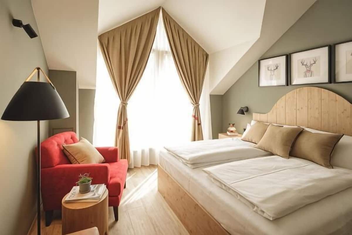 Une chambre à coucher avec un lit, une chaise rouge, une table de chevet avec une lampe et une fenêtre avec des rideaux.