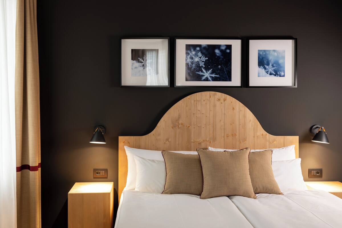 Un lit bien fait, avec une literie blanche et beige, une tête de lit en bois et trois tableaux encadrés accrochés au mur.