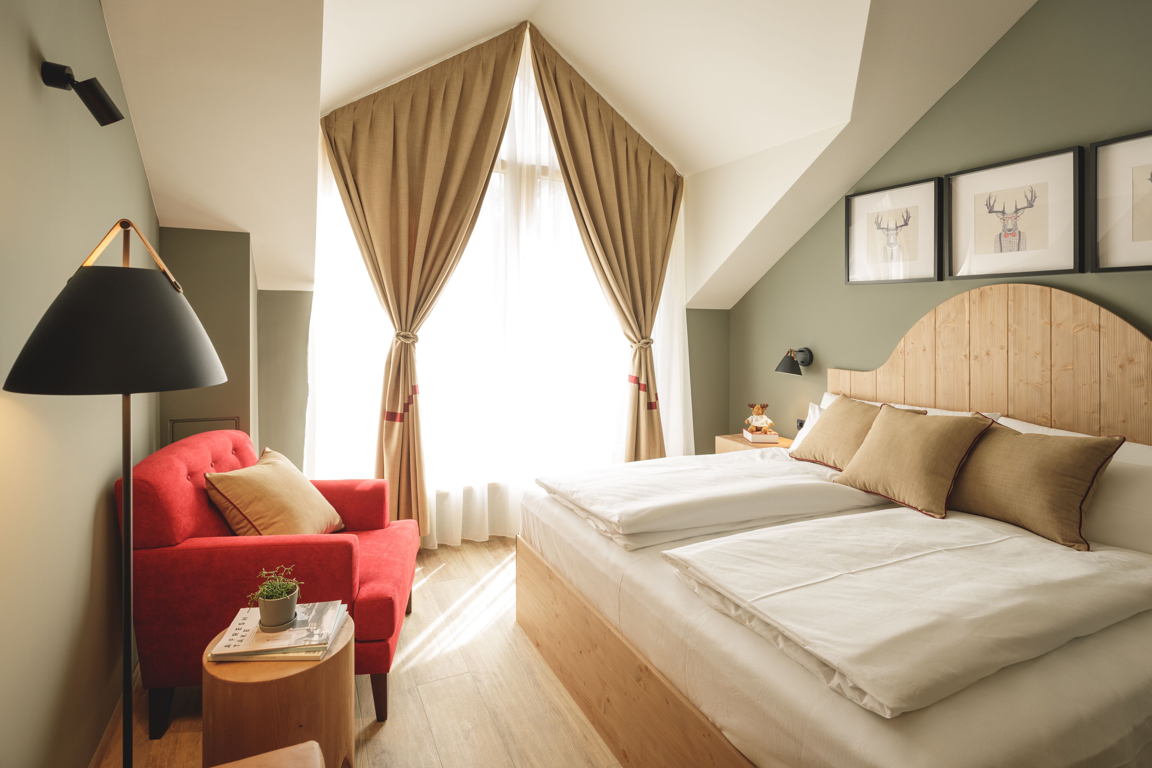 A bedroom with a bed, a red armchair, a bedside table with a lamp, and a window with curtains.