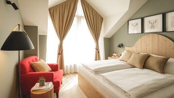 A bedroom with a bed, a red armchair, a bedside table with a lamp, and a window with curtains.