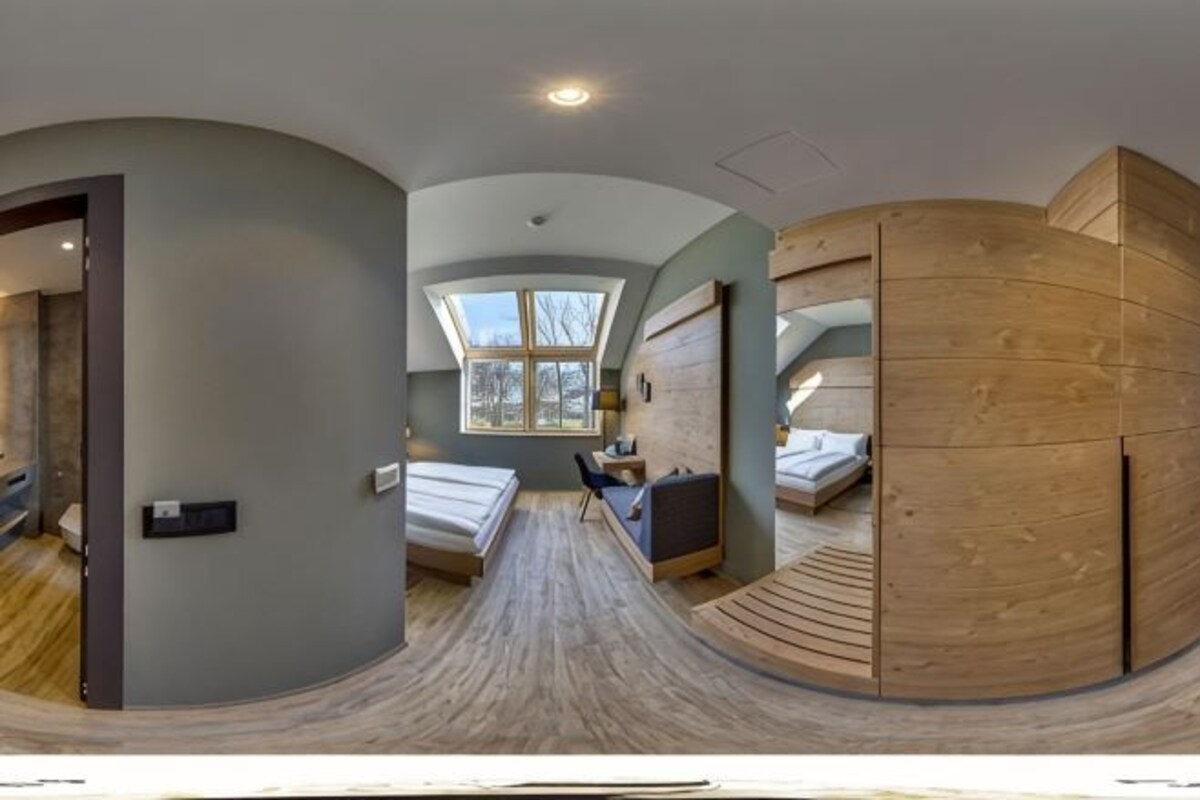 Una habitación moderna con techo curvo, tragaluz, cama, escritorio y una partición de madera curvada.