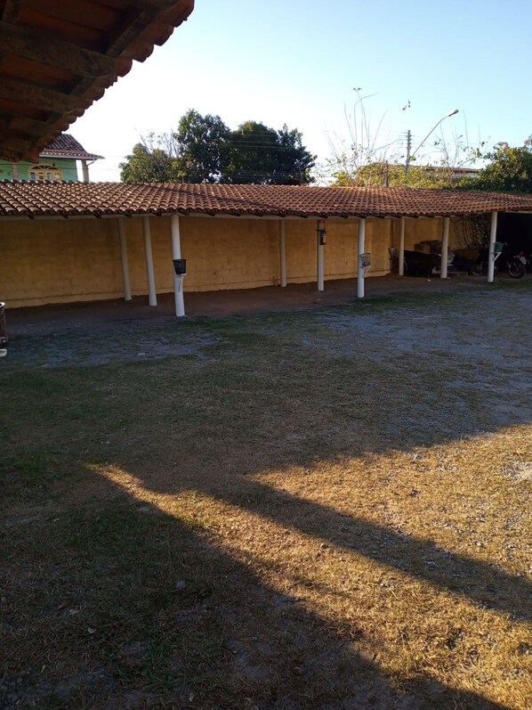 A covered outdoor area with a tiled roof, a grassy lawn, and a building with a yellow wall and a tiled roof. - Hotel Pousada Caminho da Praia (Guarapari)