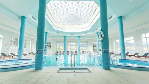 An indoor swimming pool with a skylight, blue-tiled columns, and sun loungers.