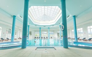 An indoor swimming pool with a skylight, blue-tiled columns, and sun loungers. - El Mouradi Hammam Bourguiba (Ain Draham)