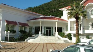 A white building with a red-tiled roof, a central entrance with steps, and a palm tree in front.