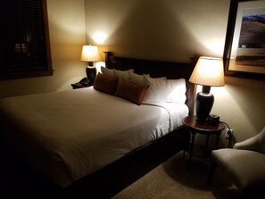 Una camera d'albergo con un letto ben rifatto, due lampade ai comodini, una sedia e un tavolino con lampada.