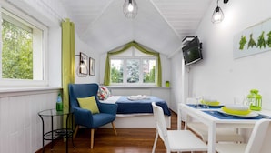 Ein gemütliches Zimmer mit einem Bett, einem Esstisch mit Stühlen, einem kleinen Tisch mit einem Sessel und einem Fenster mit Vorhängen.