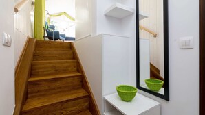 Eine Holztreppe führt zu einem Raum mit einer weißen Wand, einem Spiegel und einem grünen Korb auf einem weißen Regal.