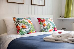 A neatly made bed with a floral pillow, a folded towel, and a white headboard. - Mokotow Cosy House Studio (Warsaw)