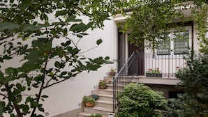 Ein Wohngebäude mit einer Treppe, die zu einem Balkon führt, umgeben von Grünpflanzen und Kübelpflanzen.