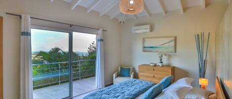 A bedroom with a bed, a dresser, a chair, and a balcony with a view.