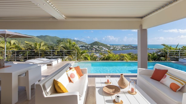 Ein Poolbereich mit weißer Möbel, Blick auf das Meer und Berge im Hintergrund.