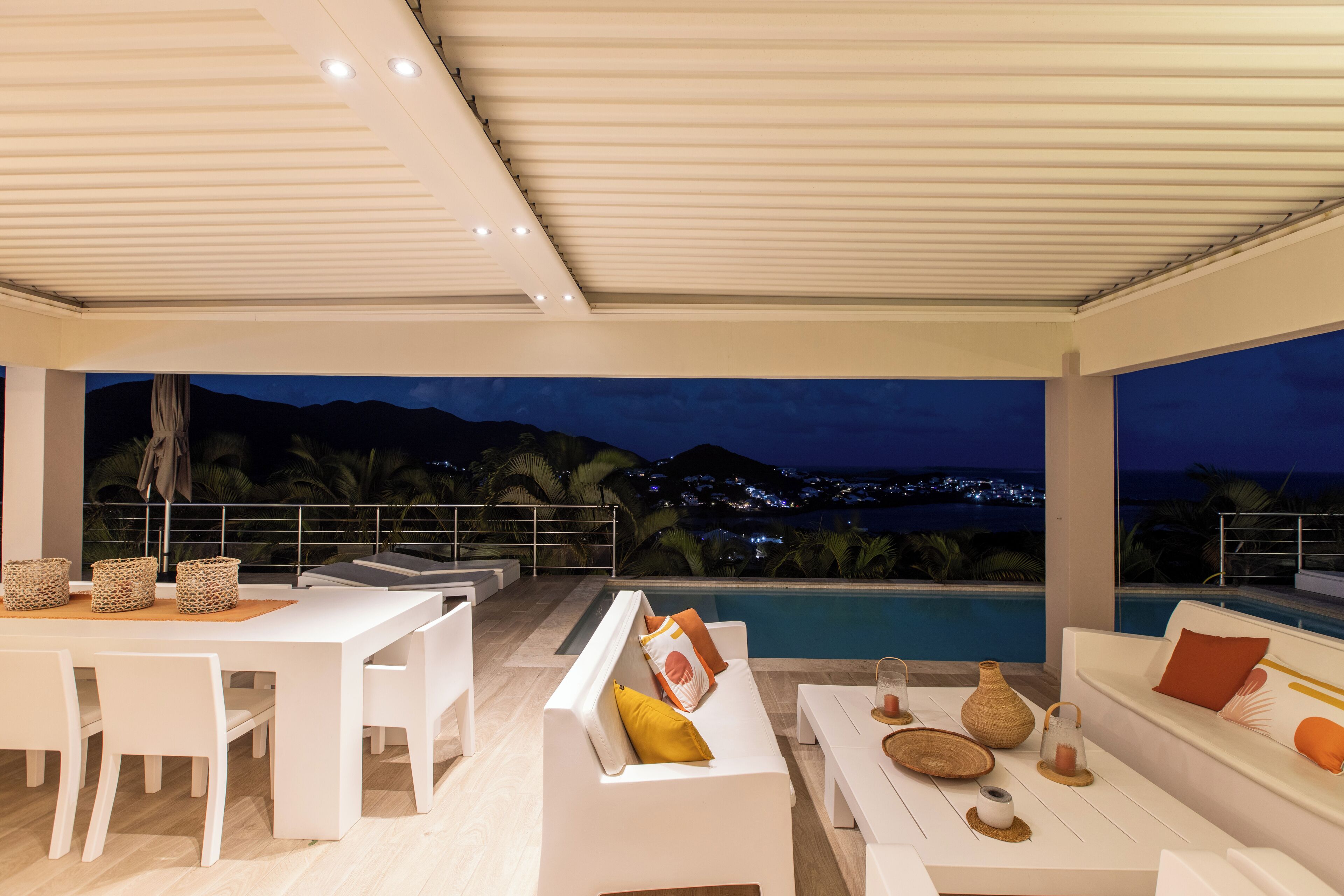 Un área de estar moderna al aire libre con vista a la piscina, mobiliario blanco y elementos decorativos.
