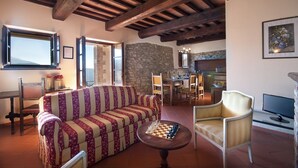 Un accogliente soggiorno con un divano a righe, un tavolino in legno e una scacchiera. Si nota una parete in pietra, una zona pranzo con sedie e una televisione.