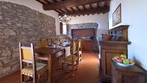 Un'area pranzo rustica con parete in pietra, travi in legno a soffitto, un lampadario e un camino in pietra.