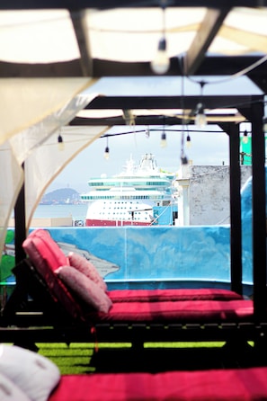 A view from inside a tent with a red cushioned seat facing a large cruise ship.