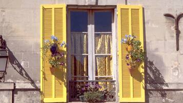 A building with yellow shutters, a window with a curtain, and potted plants with flowers.