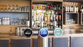 Zona de bar con estantes llenos de botellas de licor y vasos, y tres grifos de cerveza con las etiquetas Affligem, Eau y Heineken.