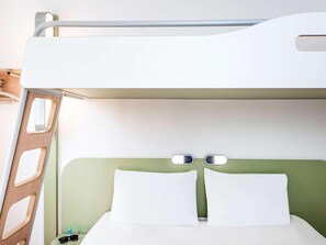 Un lit superposé avec une tête de lit verte, une literie blanche et une petite table de chevet sur laquelle se trouve un objet bleu.