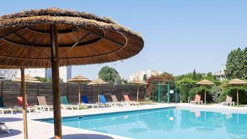 Una piscina con sillas de descanso y sombrillas de paja.