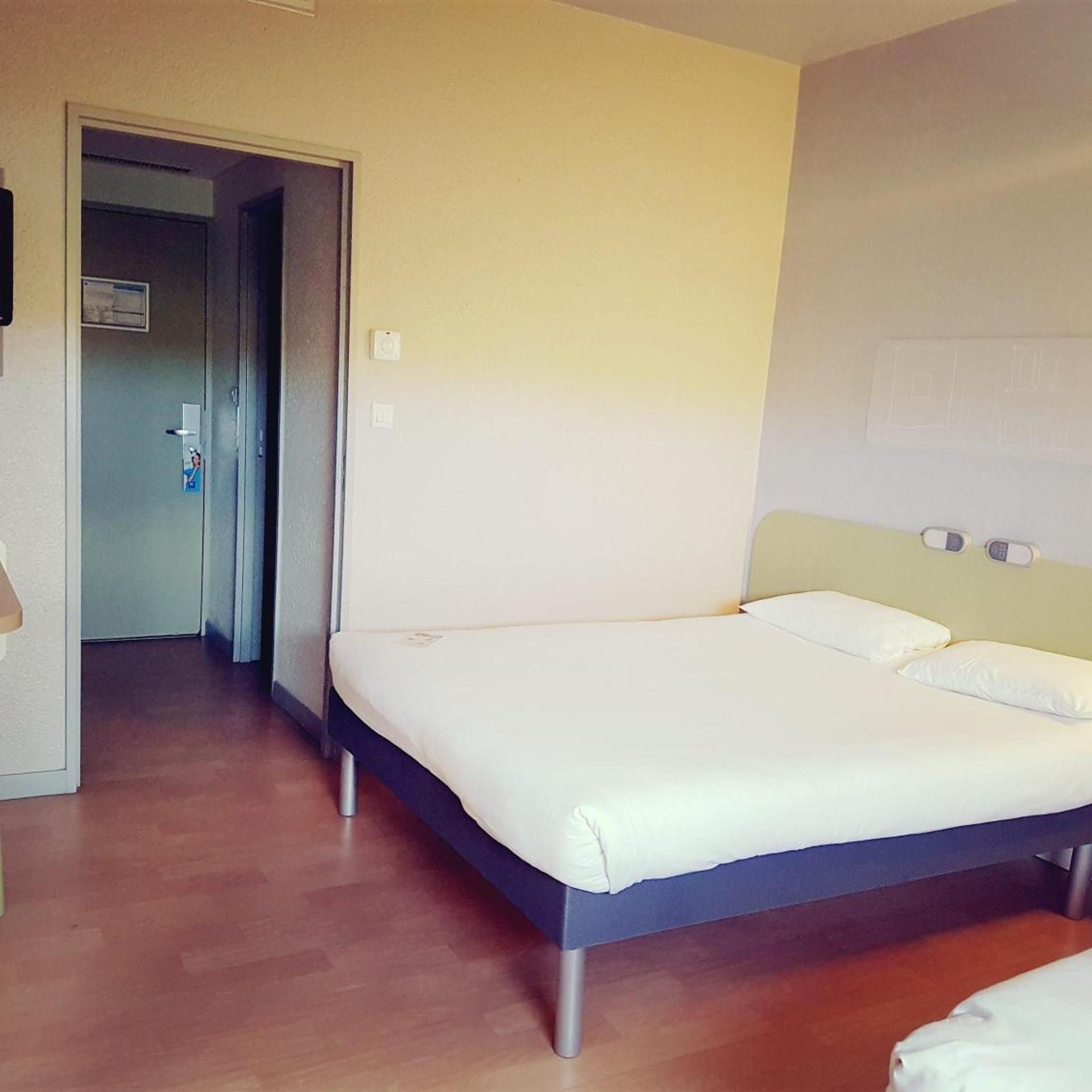 Ein Schlafzimmer mit einem Bett, einer Tür und einer Wand mit Lichtschalter.