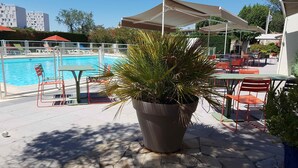 Zona junto a la piscina con una planta grande en maceta, asientos al aire libre y vista al estanque.