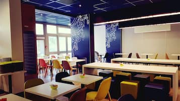 A modern dining area with multiple tables and chairs, large windows, and decorative wall art.
